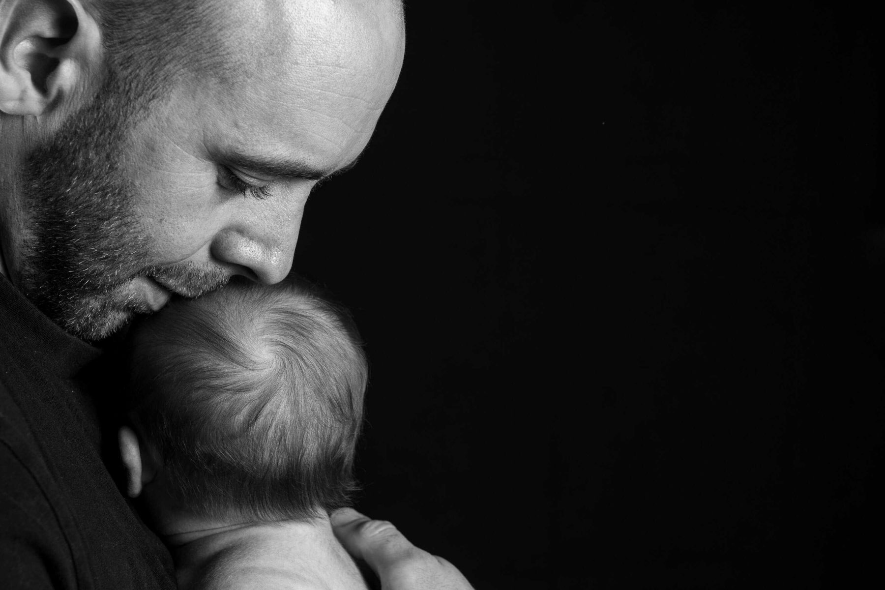 Father kissing baby's head, studio shot, black and white.