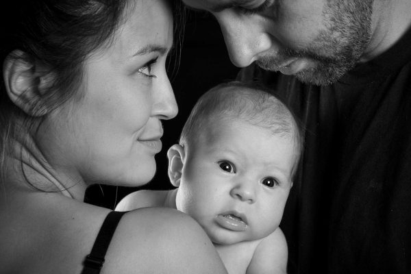 Mother, father, and baby close-up shot, studio, black and white. Baby pulling a fun expression.