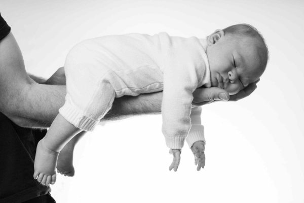 Baby on father's arms, funny shot, asleep, white background.