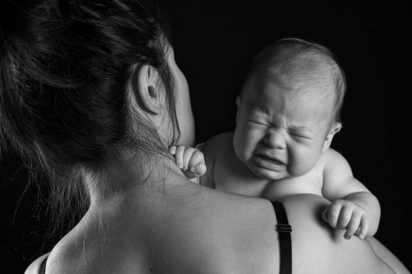 Baby crying over a mother's folder, studio shot, black and white.