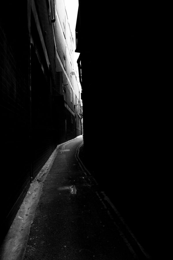 Narrow urban back alley in high contrast black and white, bright light at the far vanishing point