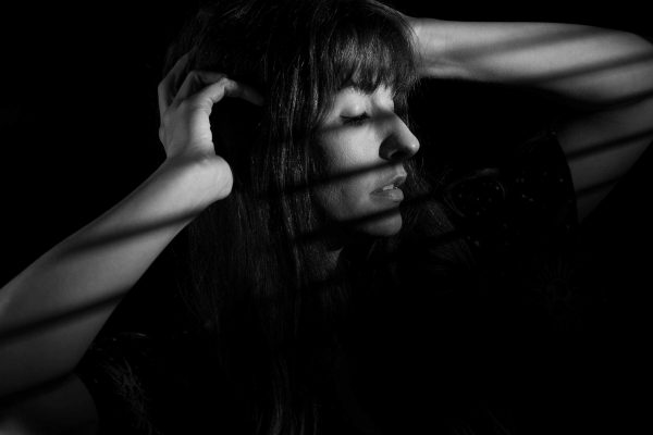 Black and white portrait of a woman looking out the window, shuttered. Shadows across her.